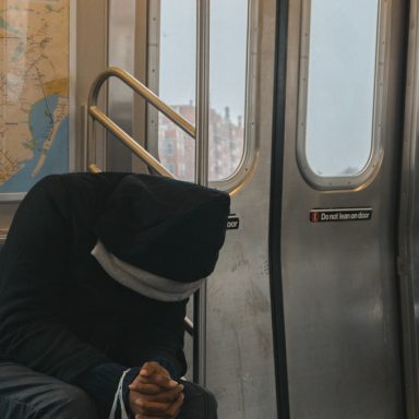 person in black hoodie sitting on train bench 362948